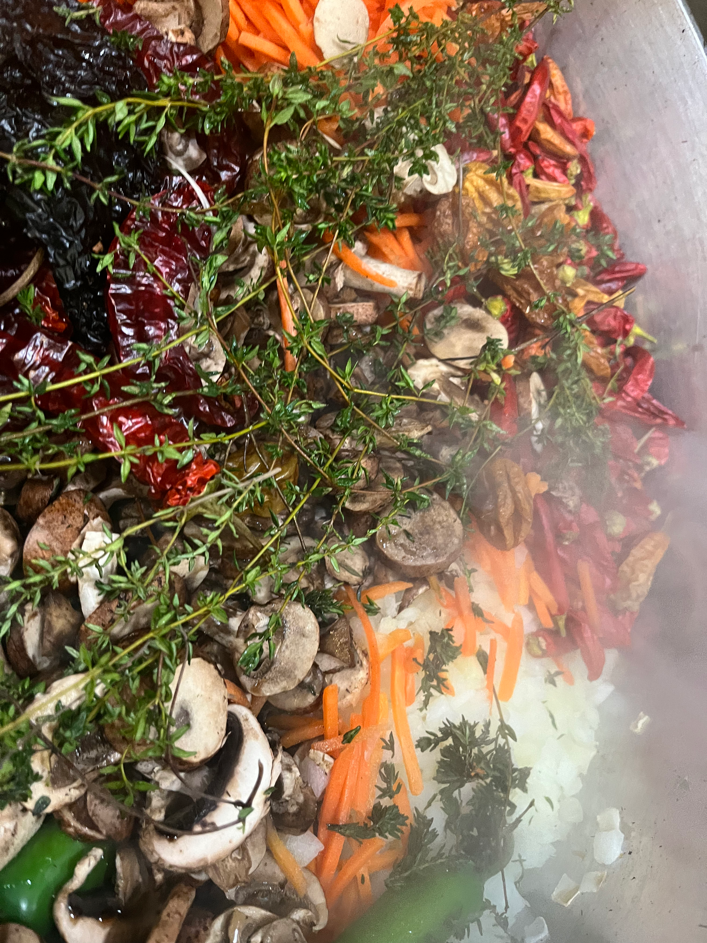 Assorted dried herbs and spices including thyme, pepper, and carrots in a metal pot.