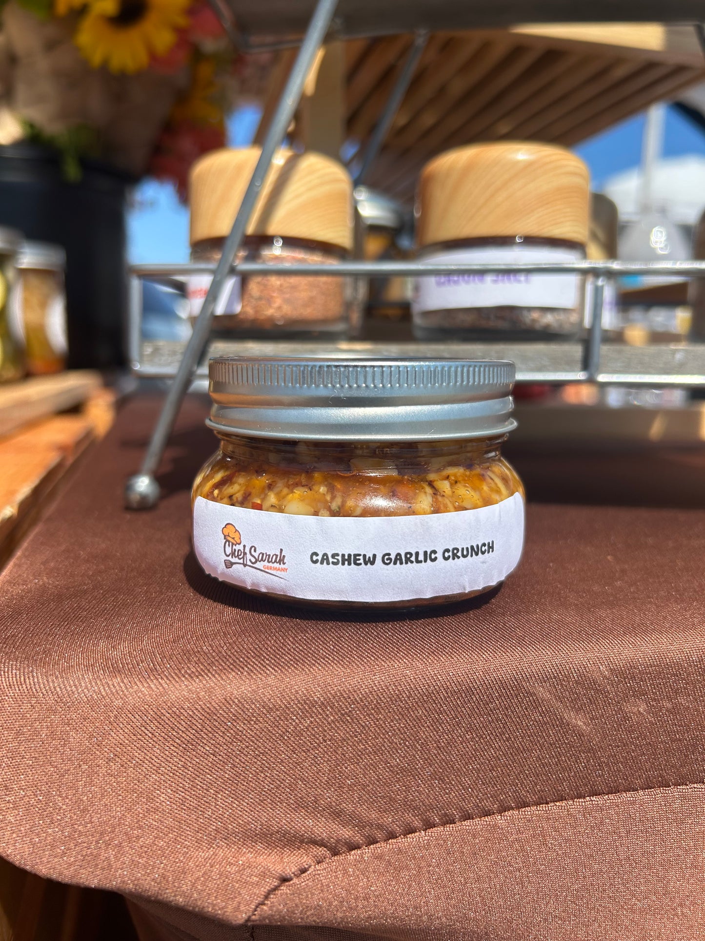 Jar of cashew garlic crunch in front of a metal rack with a brown fabric background