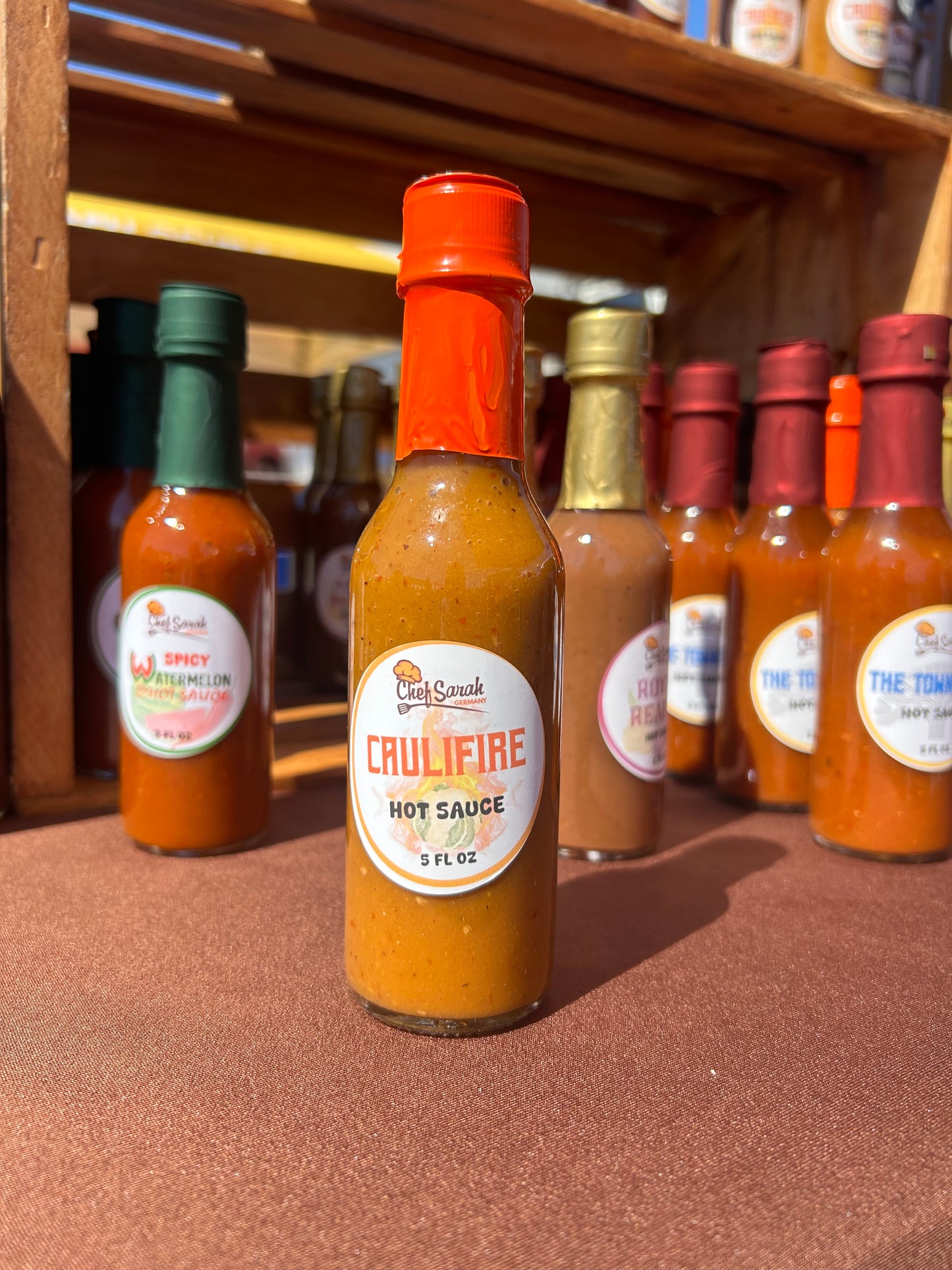 Assorted hot sauce bottles with visible labels on a brown surface. Caulifire hot sauce is centered.