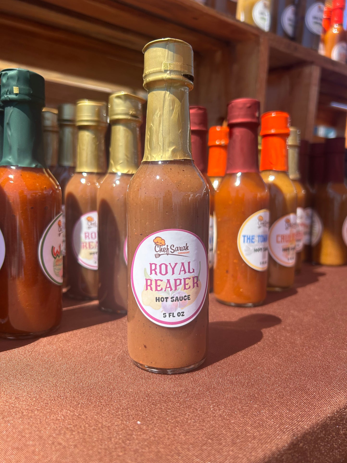 Bottle of 'Royal Reaper' hot sauce with a gold cap on a brown surface.