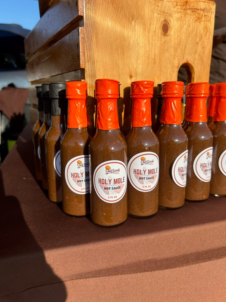 Row of Holy Mole hot sauce bottles with orange caps on a wooden stand.