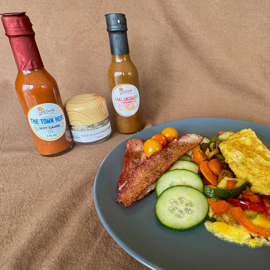 Plate of breakfast food with The Town Heat hot sauce, Oaklandshire sauce, and mushroom salt bottles on a brown background
