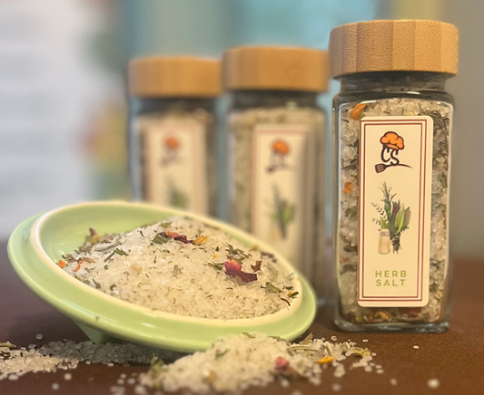 3 jars of herb salt and a green bowl of herb salt on a brown surface