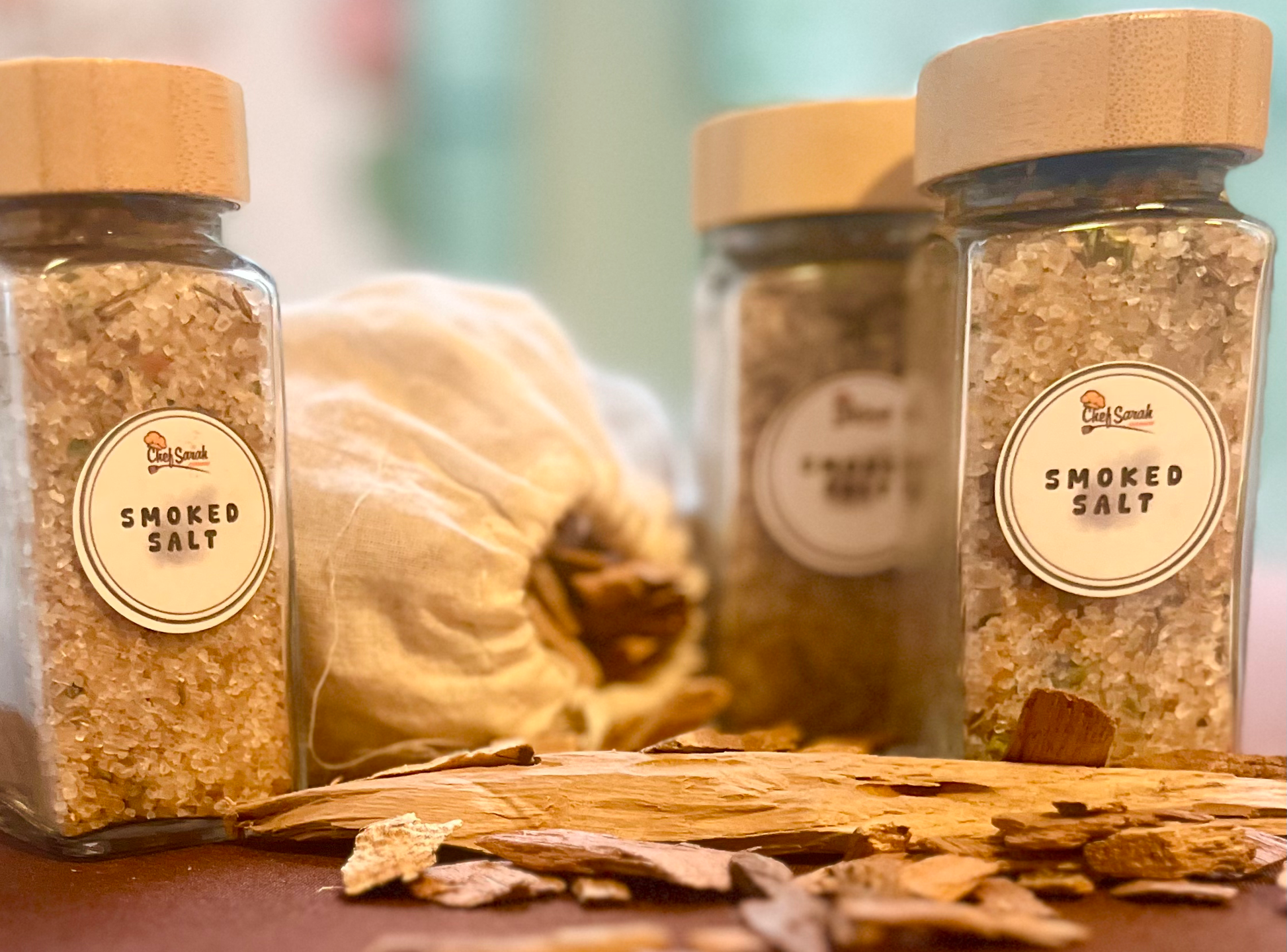 Three jars of smoked salt with wooden lids on a wooden surface.