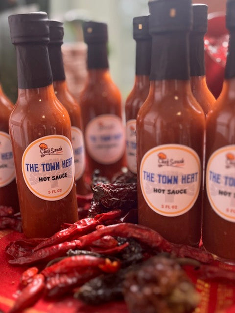 Bottles of 'The Town Heat' hot sauce with chili peppers on a red surface