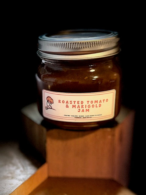 a jar of roasted tomato and marigold jam on a wooden block