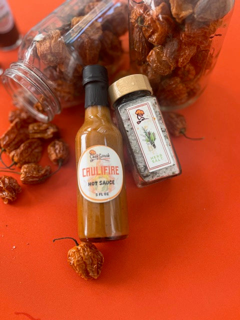 Cauliflower hot sauce bottle with a jar of dried peppers on an orange background