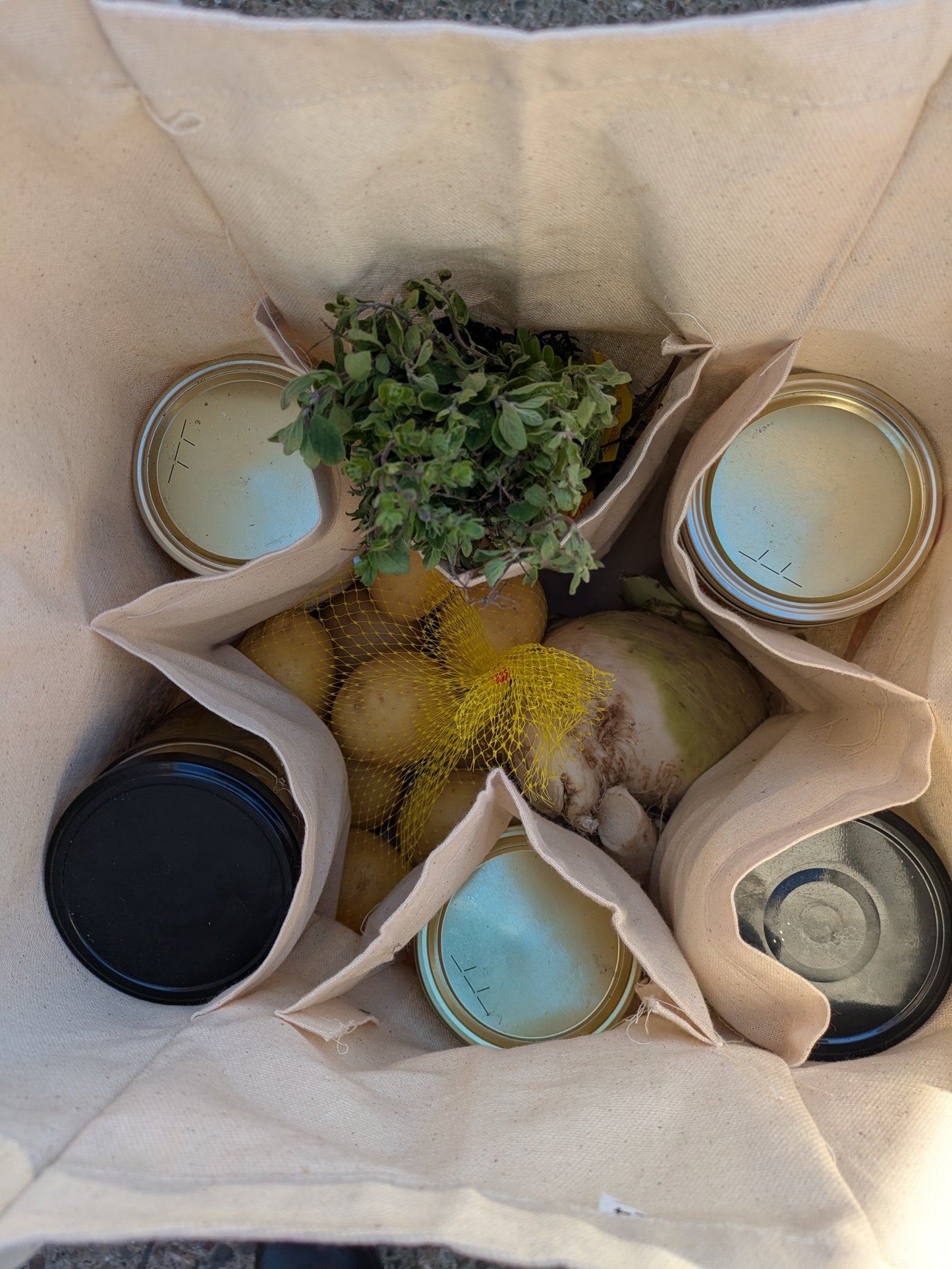 The inside of a beige tote bag. Jars in the internal pockets and vegetables in the center.